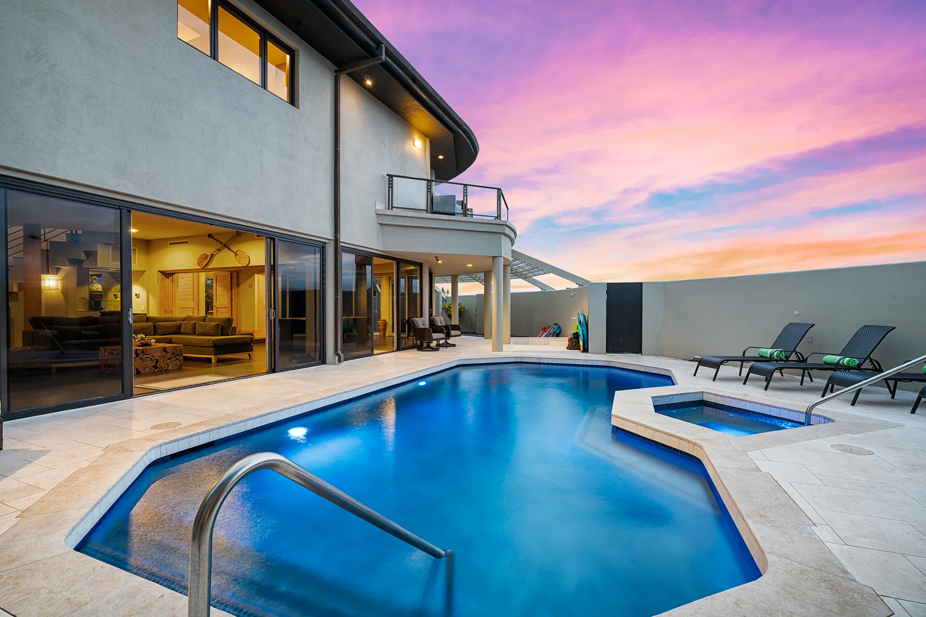 A swimming pool beside a modern house, with lounge seating and a colorful sunset sky.
