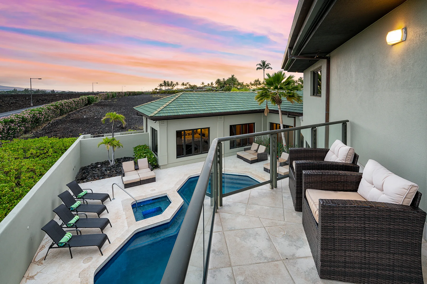 A rooftop terrace overlooks a swimming pool and landscaped courtyard at sunset.