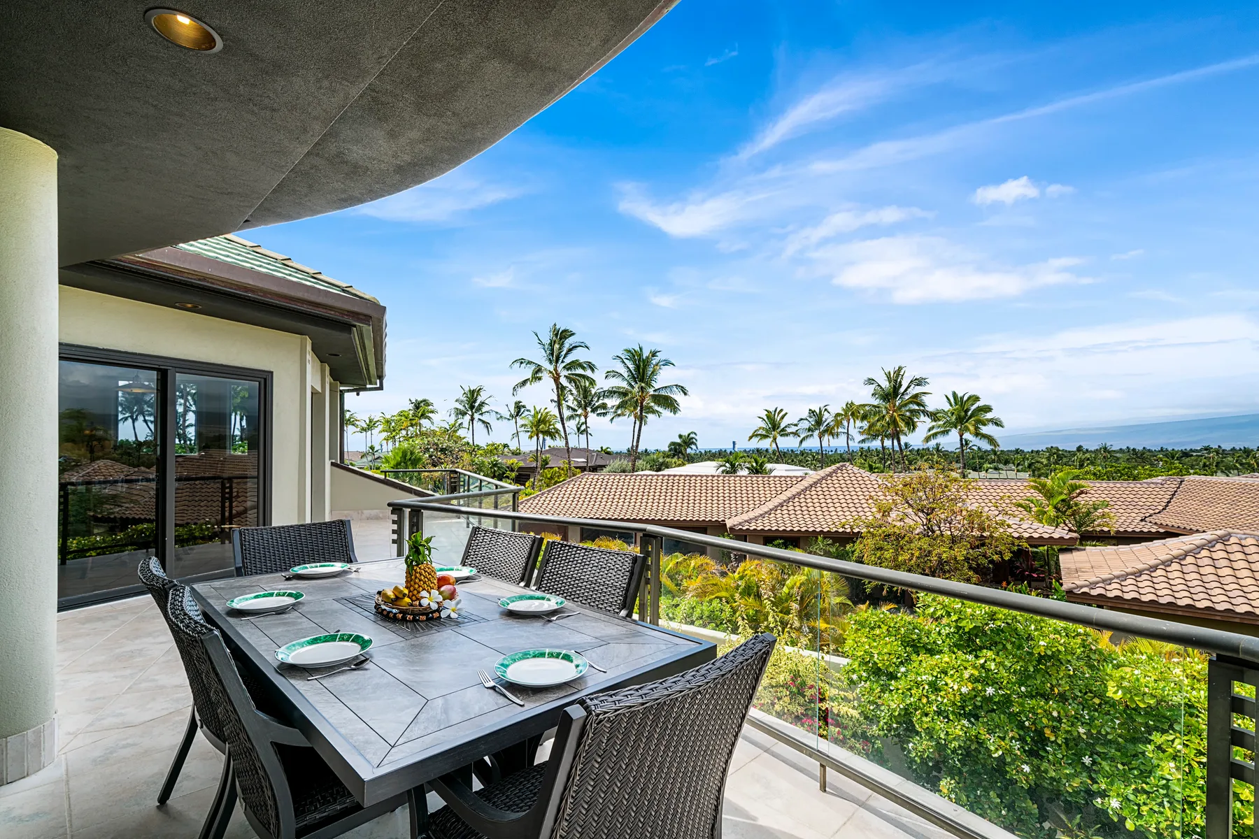 A balcony dining area overlooks palm trees and rooftops beneath a blue sky.
