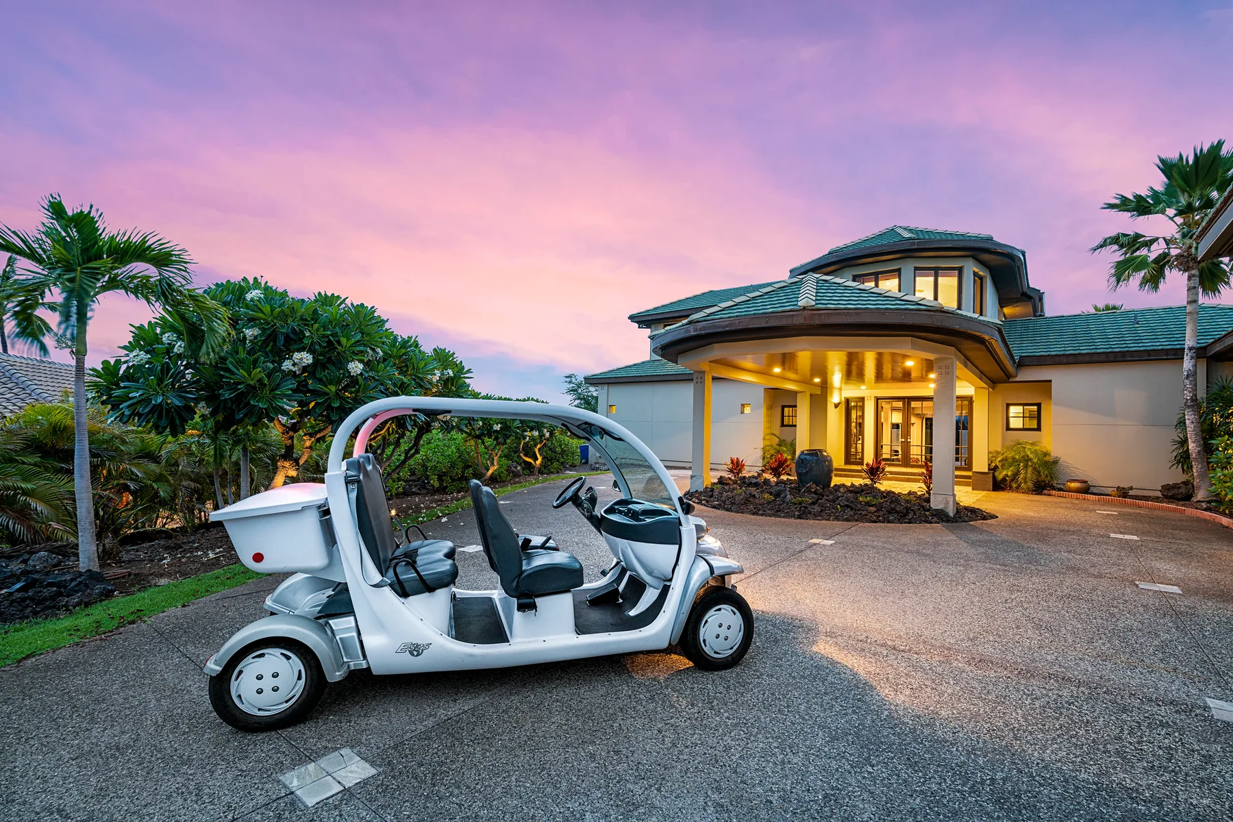 A golf cart is parked in front of a warmly lit house at dusk.