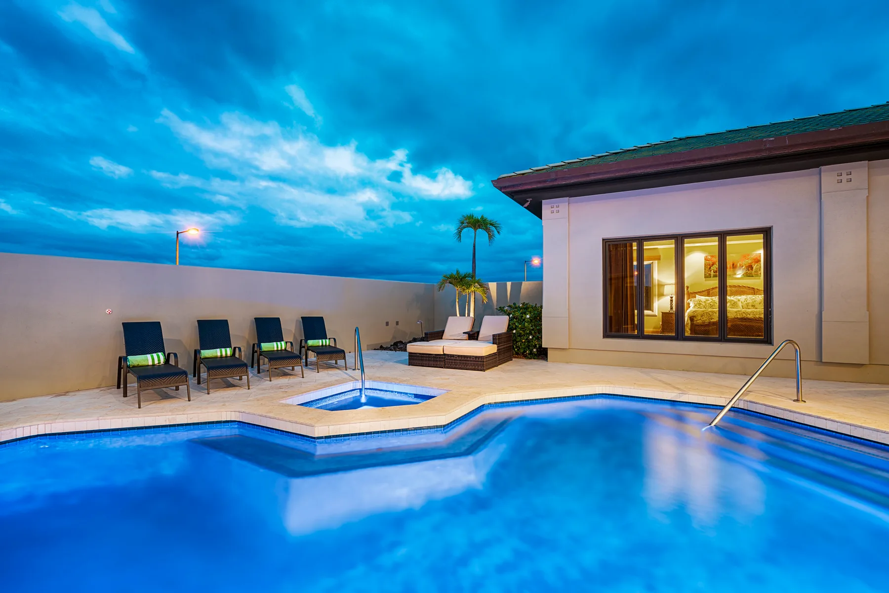 An outdoor pool beside a patio seating area and a brightly lit building.