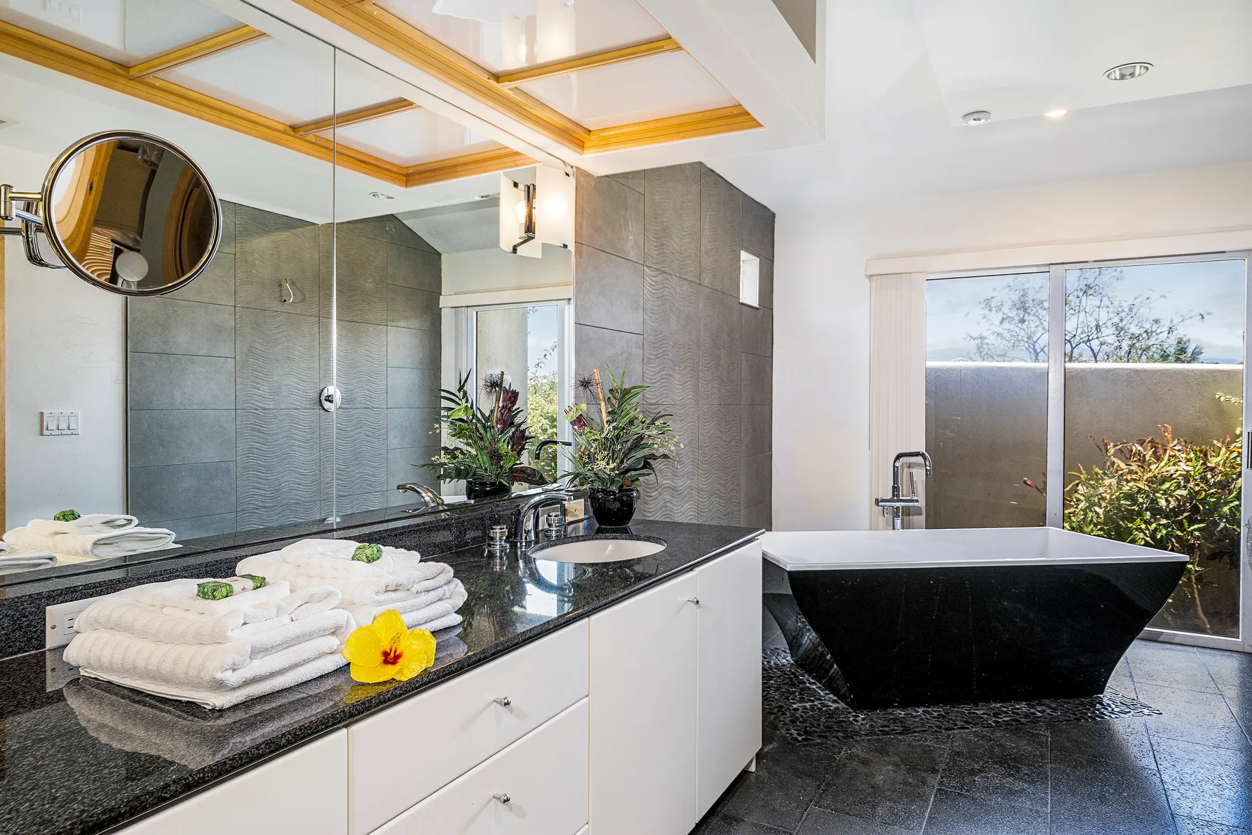 A modern bathroom with a black bathtub, wide vanity, and large window.