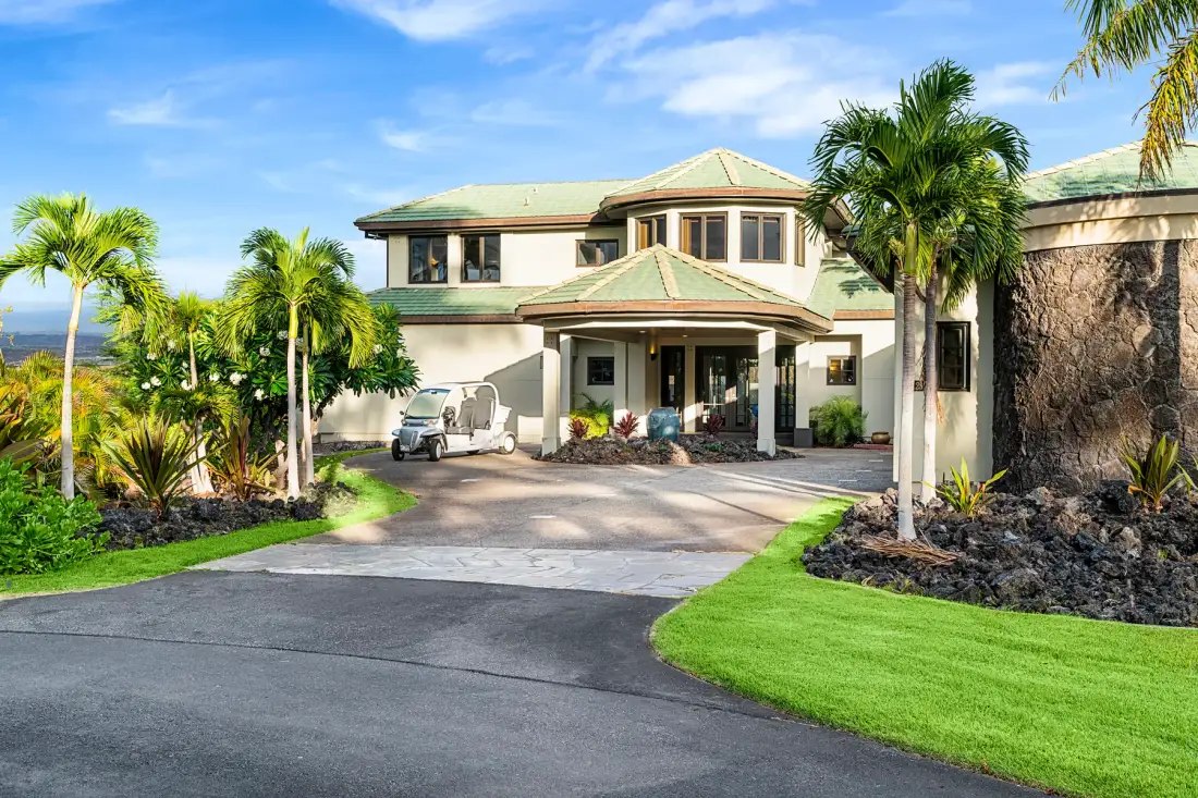 A large house with a covered entrance, palm trees, and landscaped grounds.