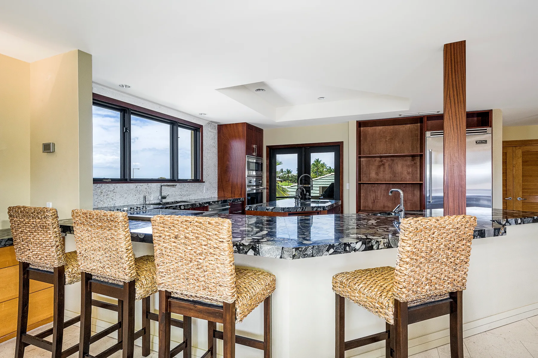 A spacious kitchen with a dark stone island and woven bar seating.