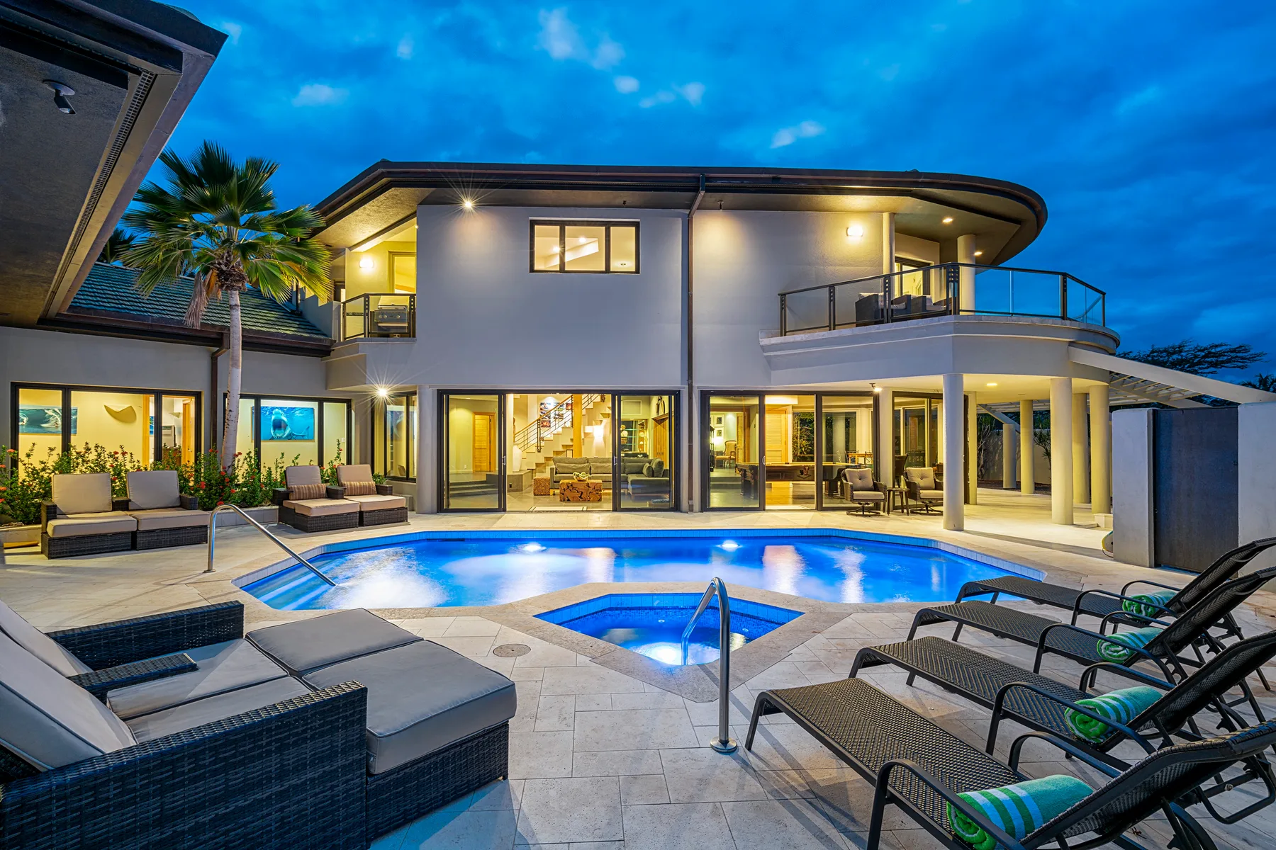 A modern house opens onto a swimming pool surrounded by lounge seating.