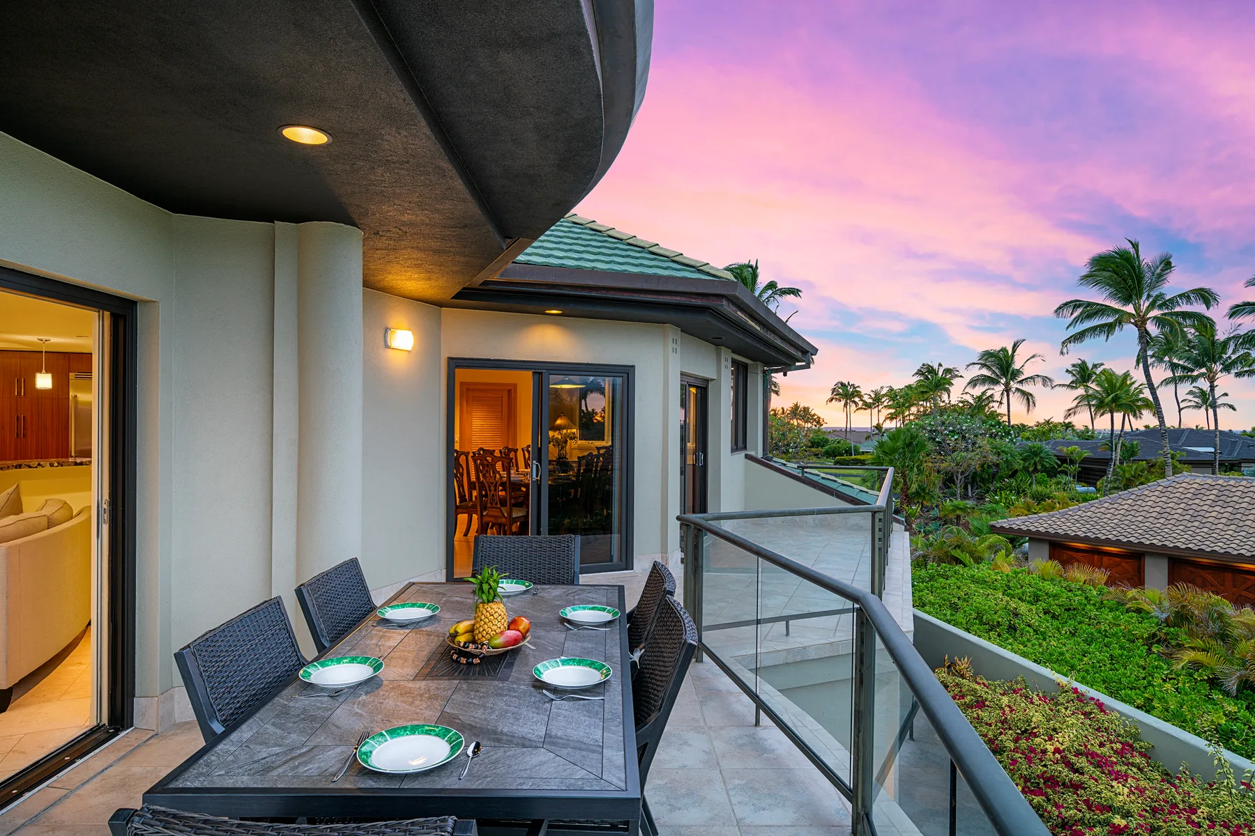 An outdoor dining area overlooks palm trees and neighboring rooftops at sunset.