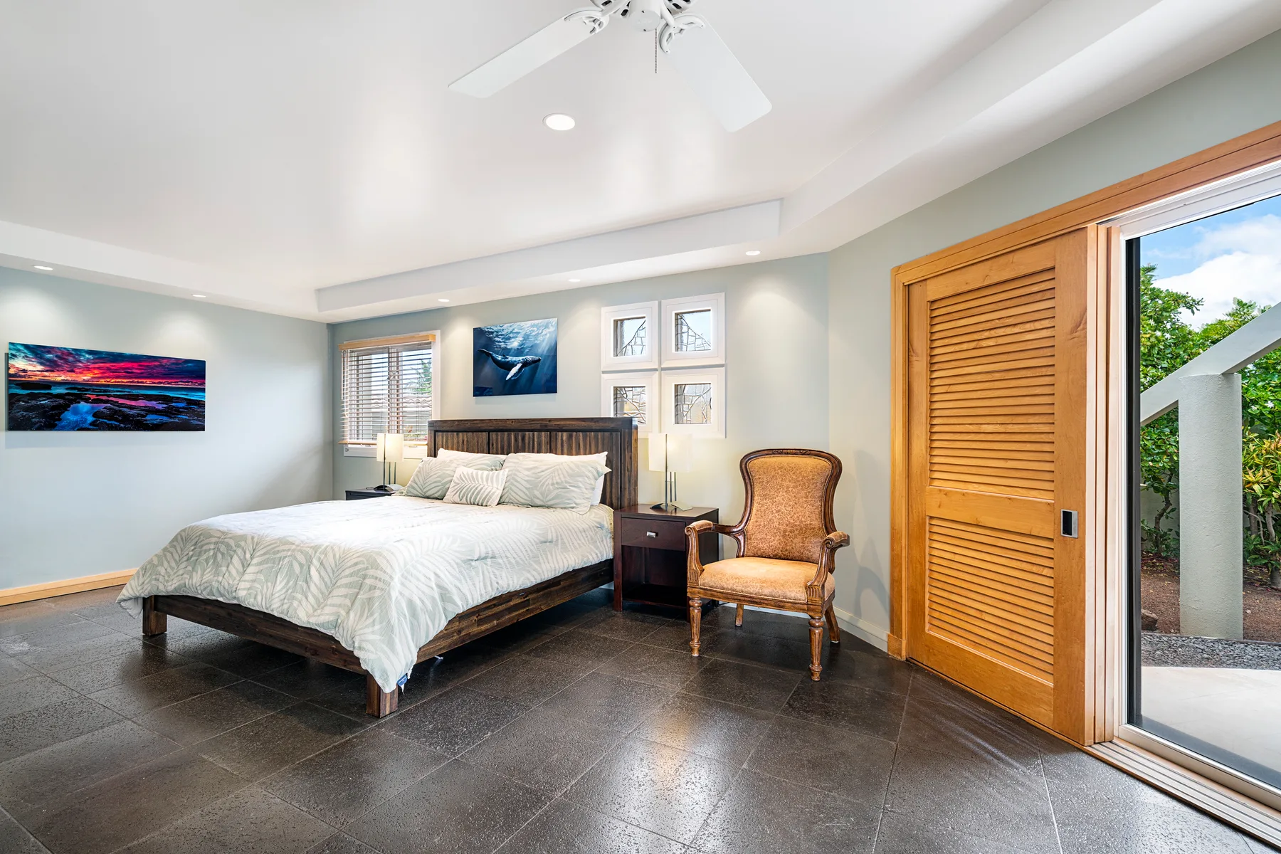 A bedroom with a bed, a chair, and a sliding glass door opening to greenery.