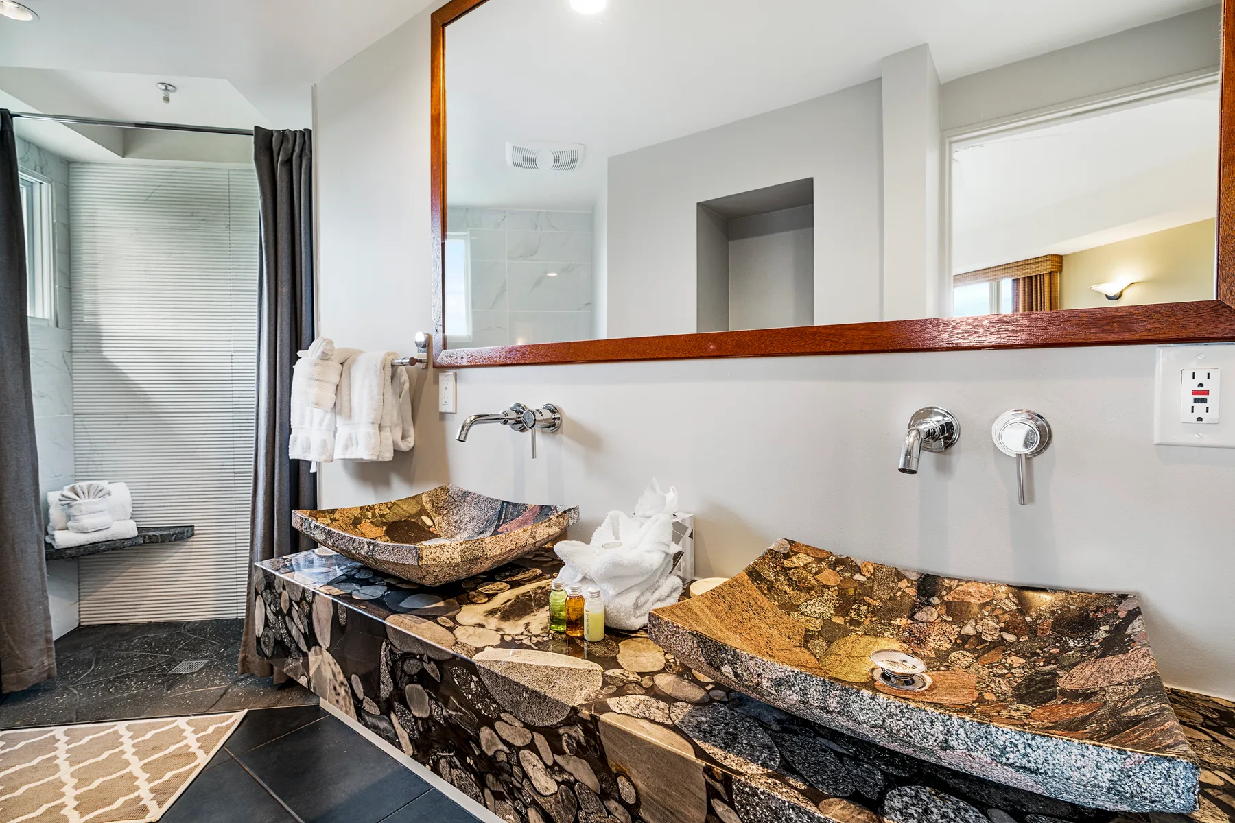 A bathroom vanity with two stone vessel sinks and a large mirror.