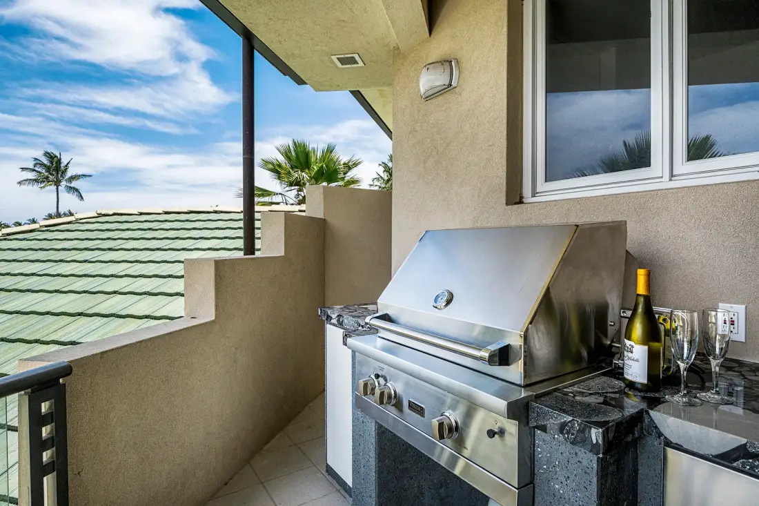 A stainless-steel grill sits on a tiled balcony beside a window.