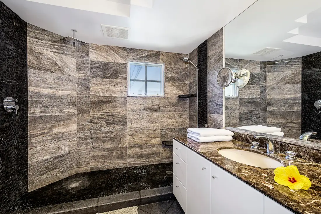 A tiled bathroom with a glass shower area and a vanity beside the sink.