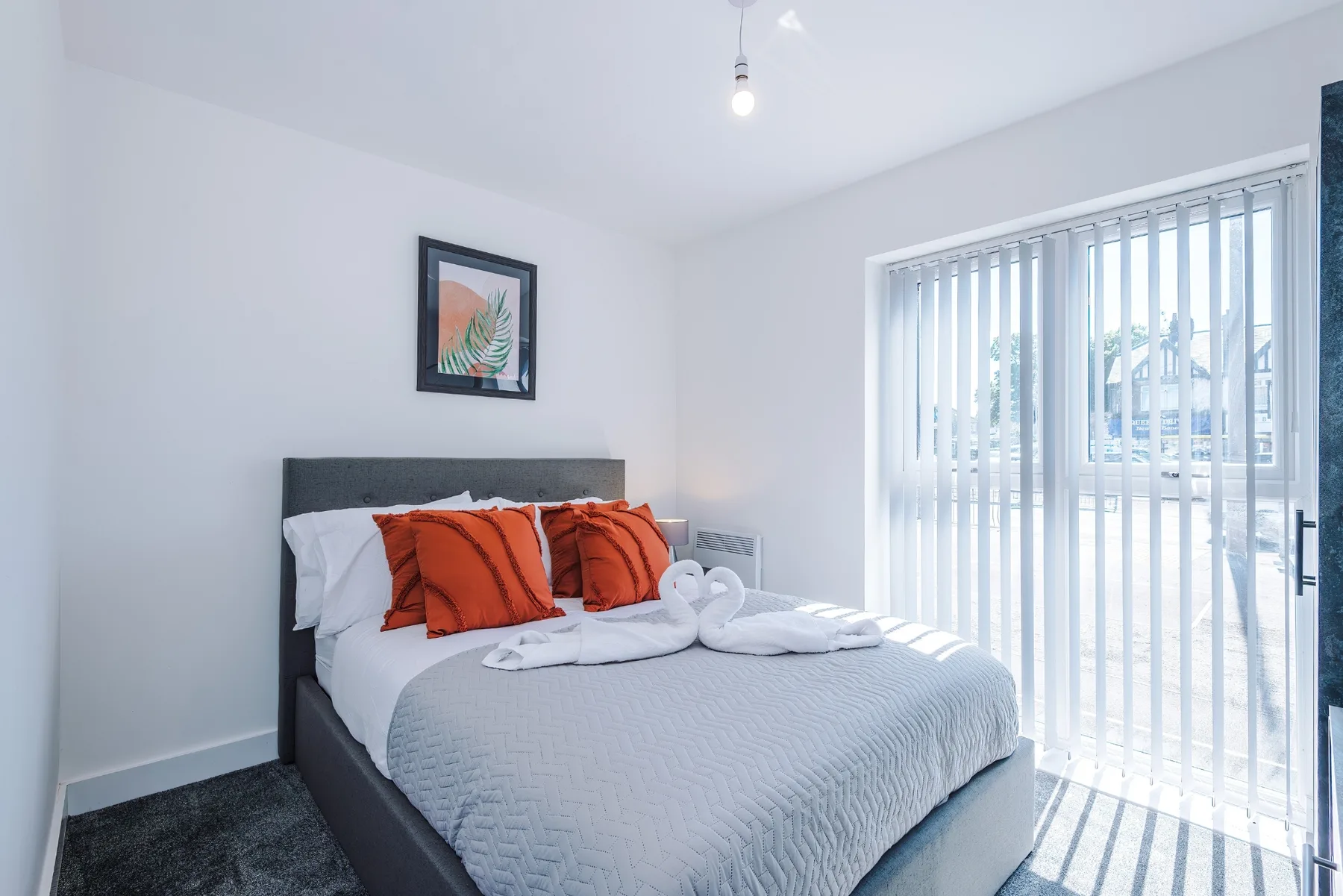 Un dormitorio con la cama tendida y persianas verticales frente a las puertas de vidrio.