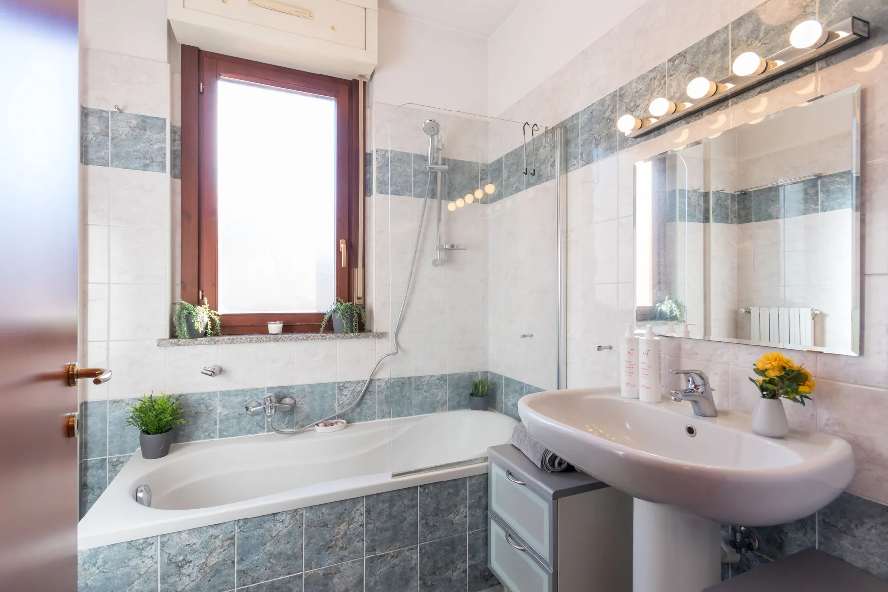 Un baño alicatado con bañera, ducha y lavabo bajo un espejo grande.