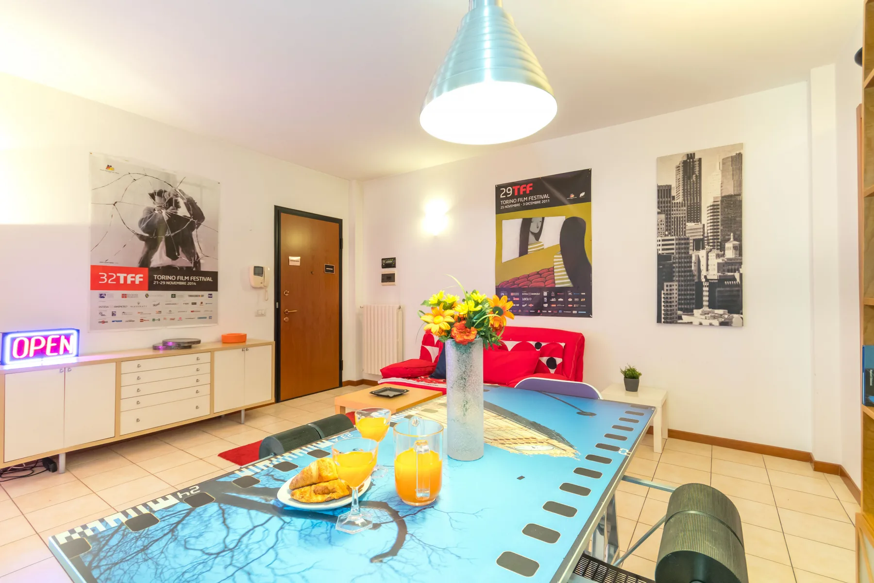 Un comedor luminoso con una mesa larga, sillas de colores y carteles en las paredes.