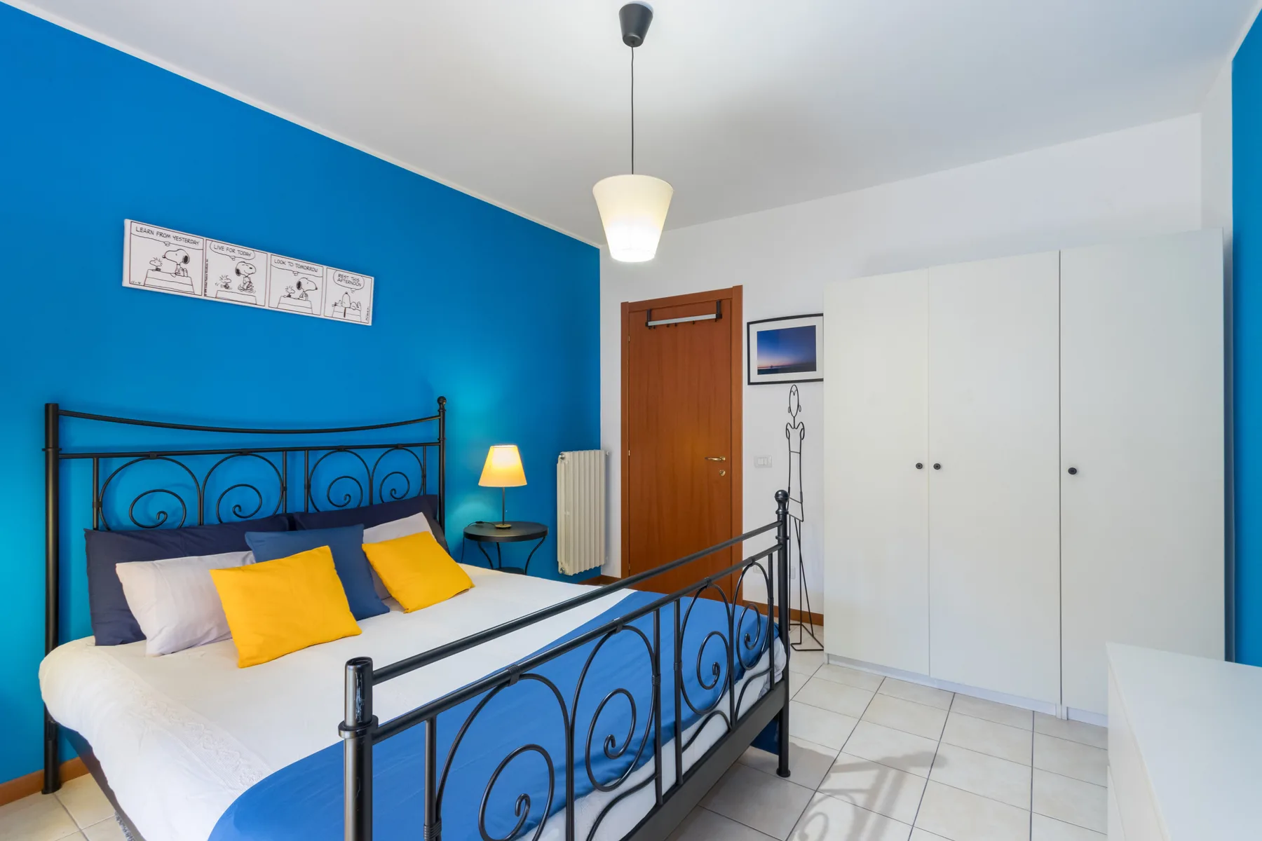 Un dormitorio con una cama de metal negro, una pared azul y armarios blancos.