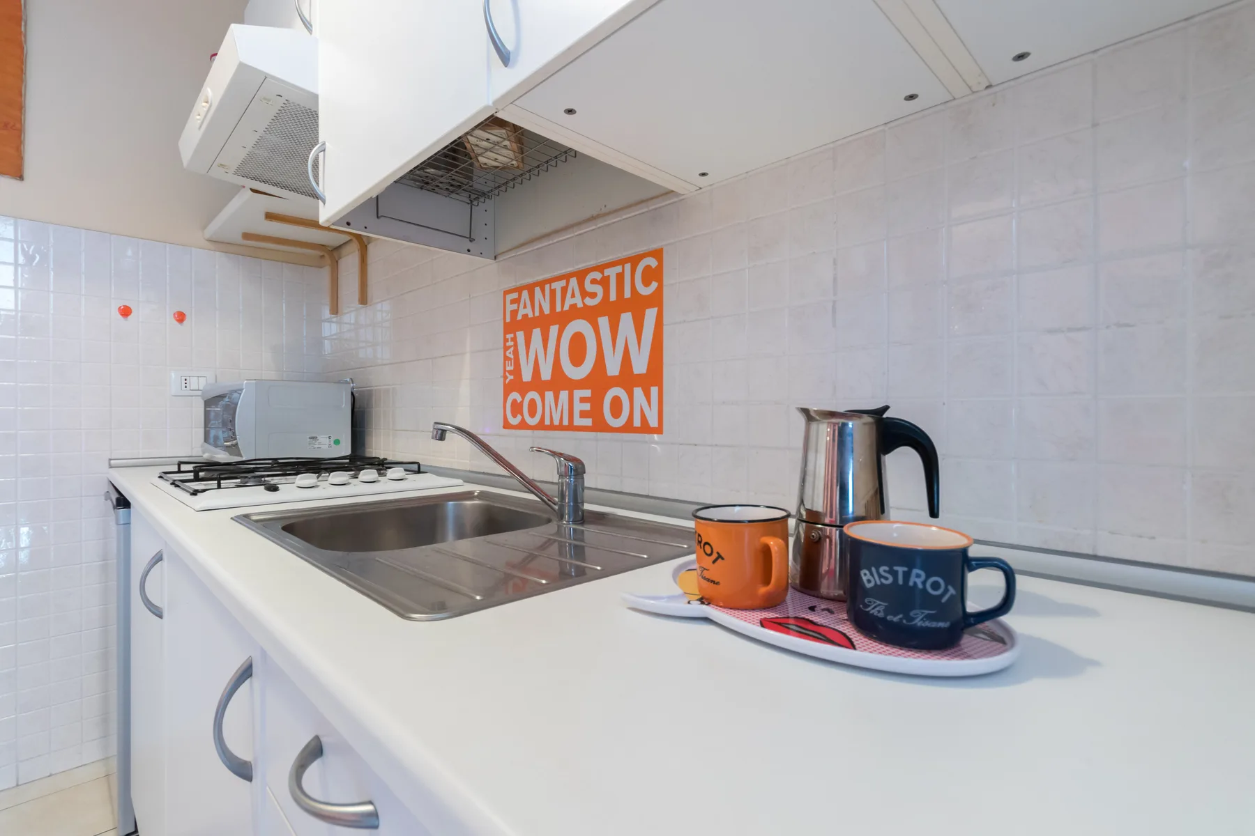Una cocina luminosa con estufa, fregadero y tazas sobre la encimera.