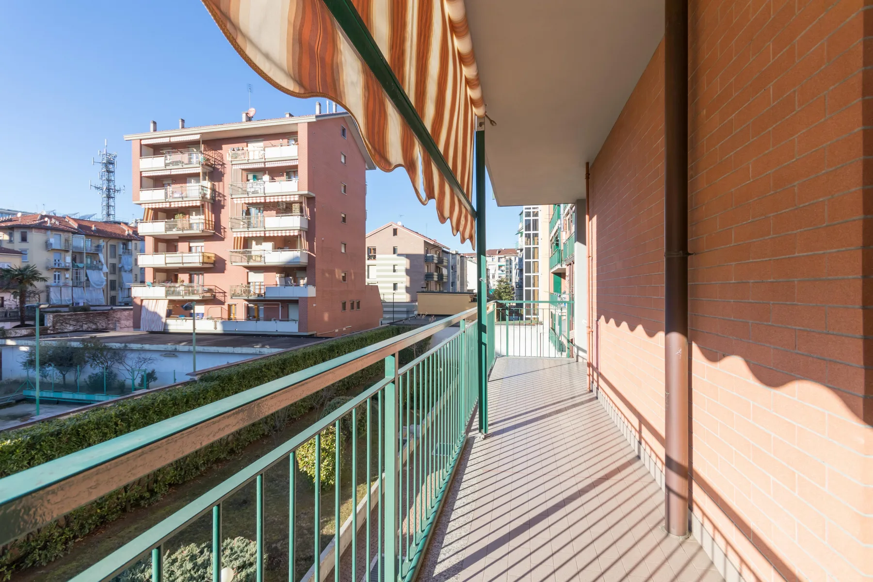 Un pasillo de balcón con barandilla verde da a edificios de apartamentos cercanos.