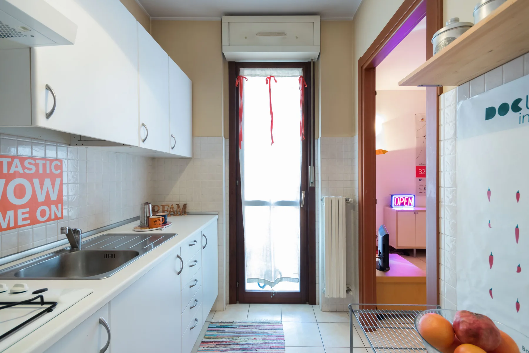 Una cocina estrecha con armarios blancos, una encimera y una puerta acristalada alta.