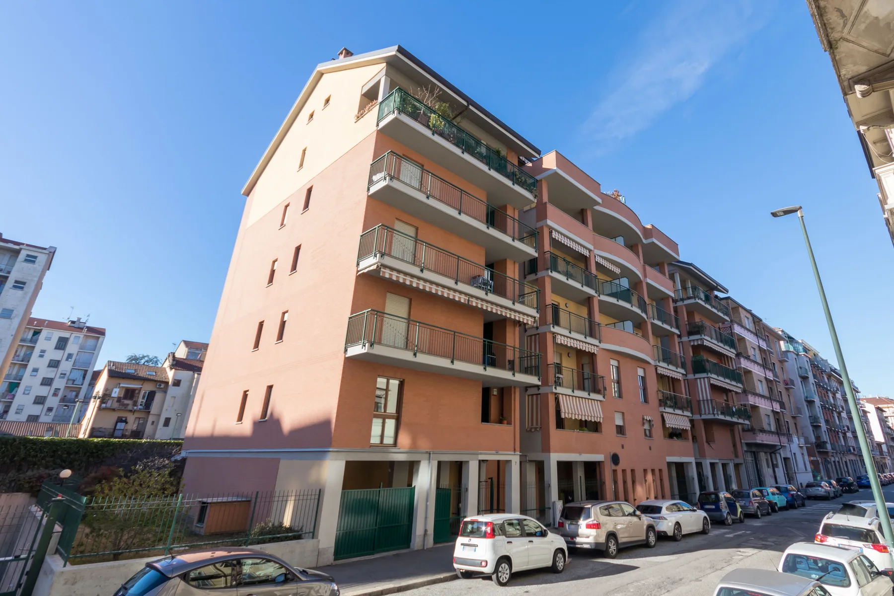 Una hilera de edificios de apartamentos con balcones bordea una calle urbana soleada.