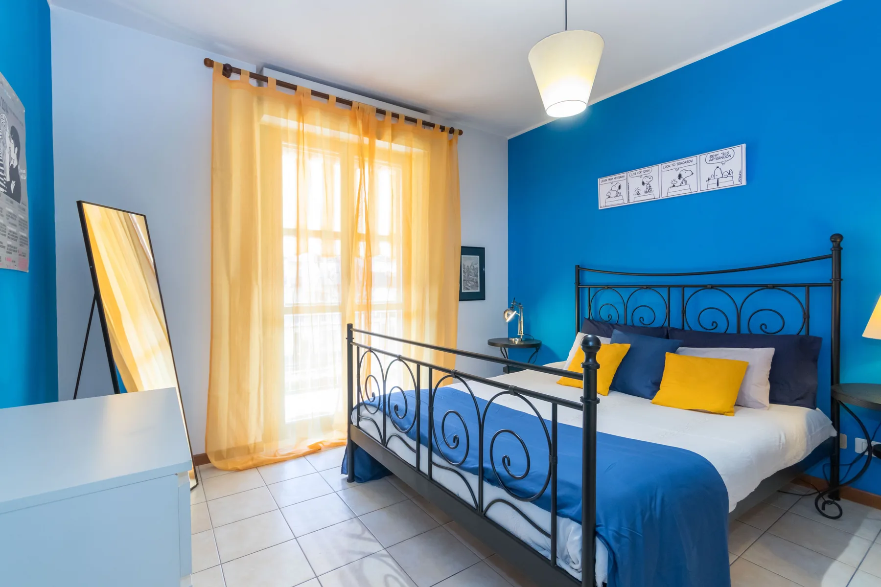 Un dormitorio con ropa de cama azul, estructura metálica y una ventana iluminada.