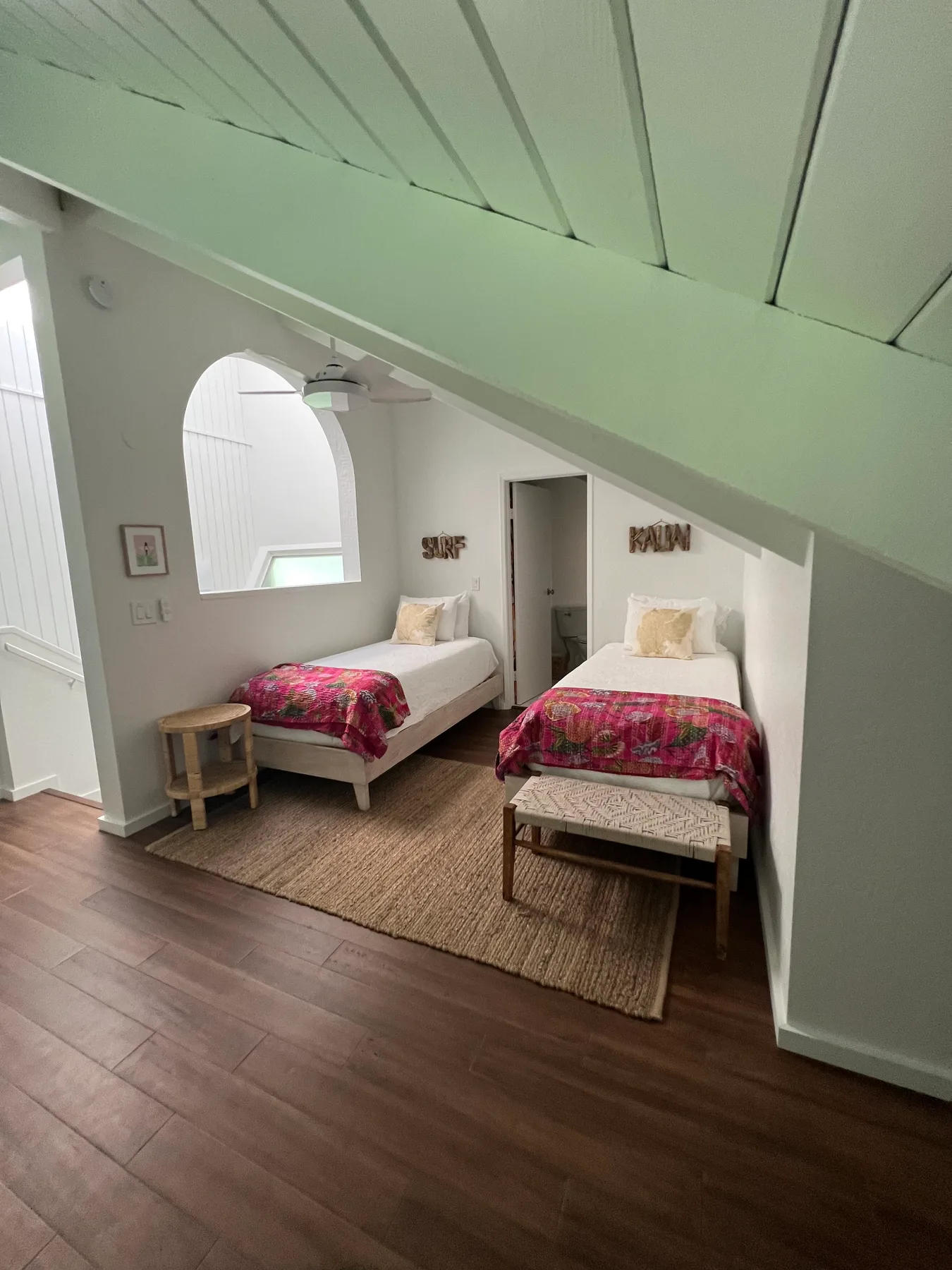 A bedroom with two beds and a woven rug beneath a sloped ceiling.
