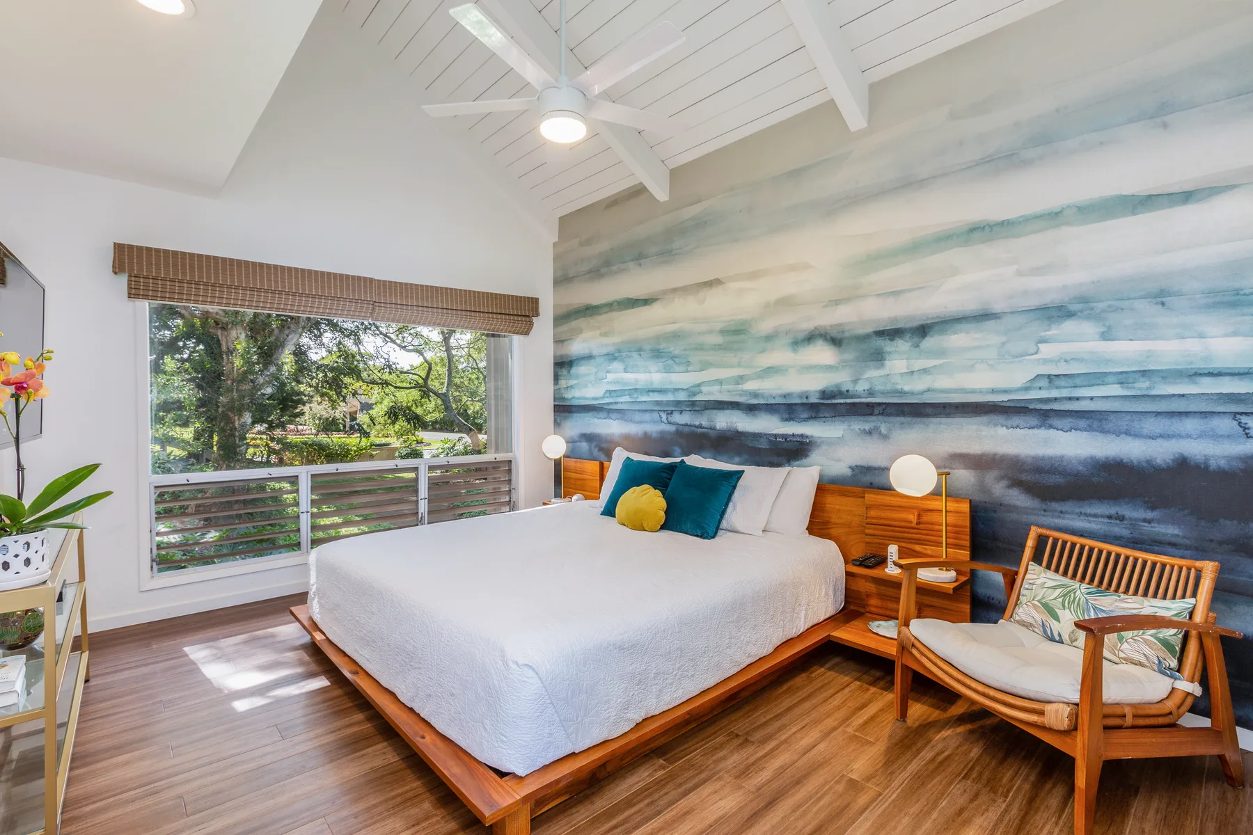 A bedroom with a large bed, a colorful wall mural, and a window overlooking greenery.