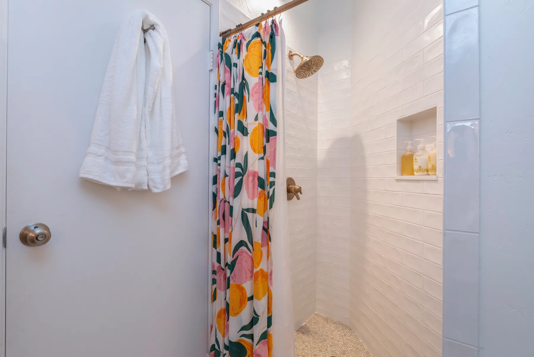 A tiled bathroom shower area with a colorful patterned curtain and a wall niche.