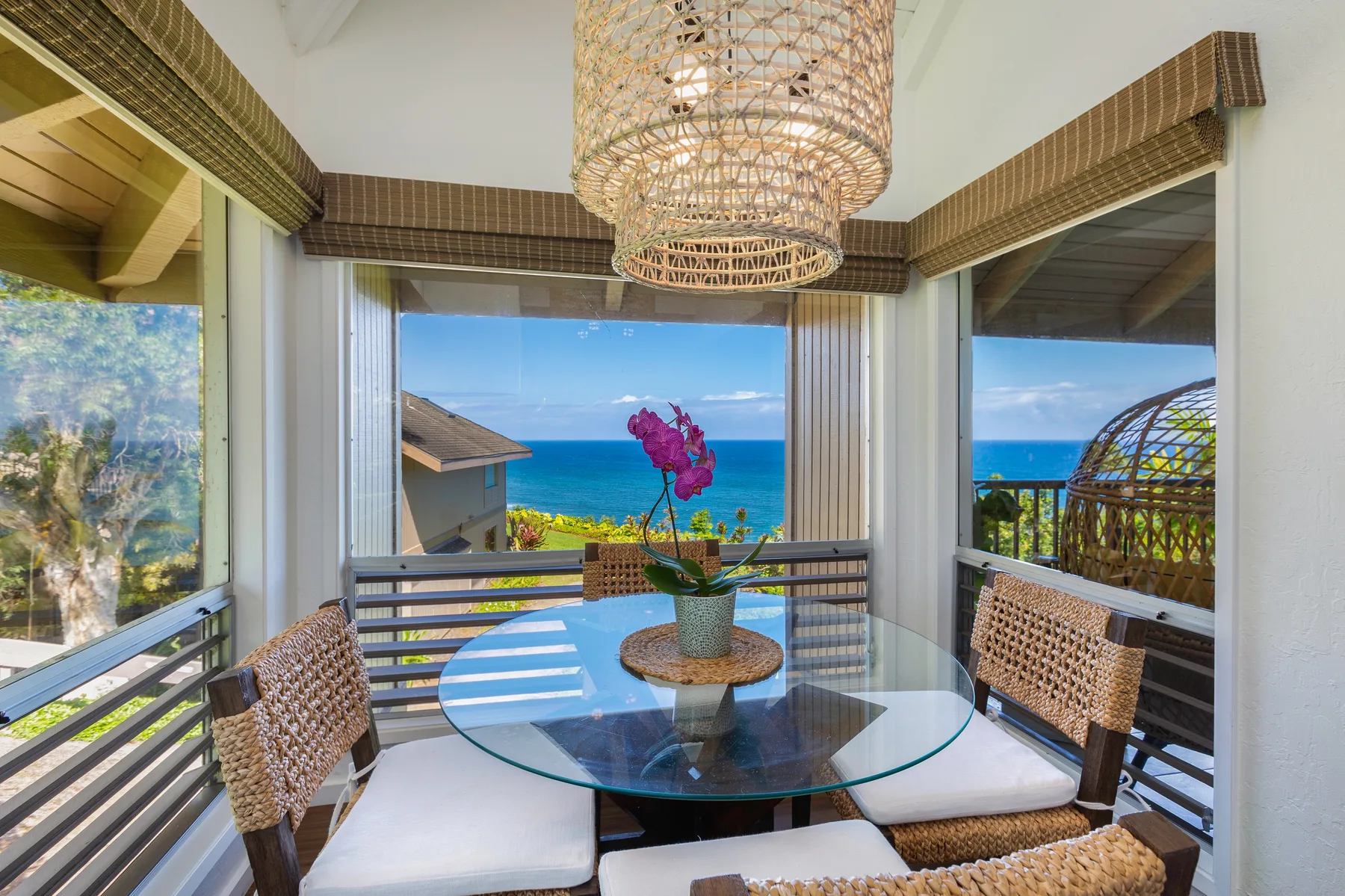 A bright balcony dining area with a glass table overlooking the ocean.