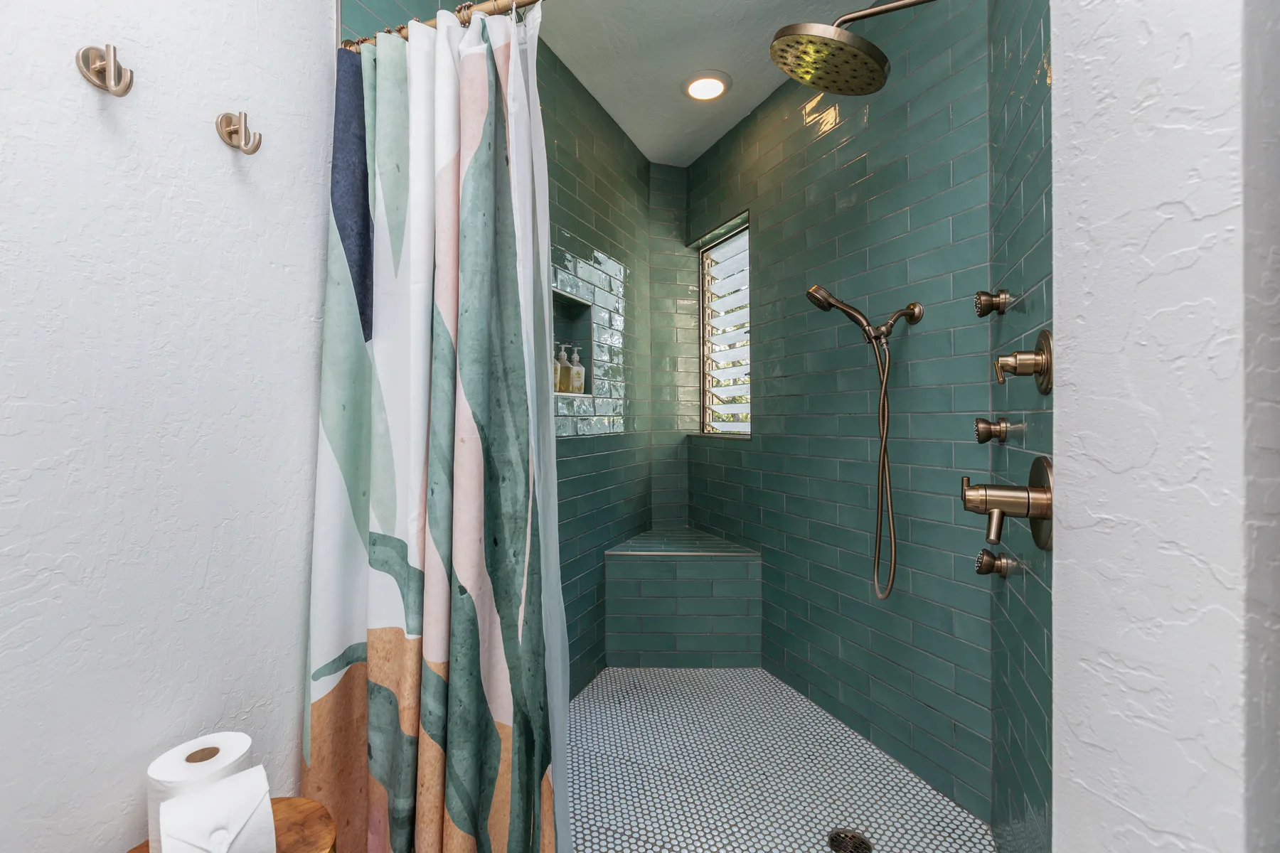 A tiled shower area with a patterned curtain and built-in bench.