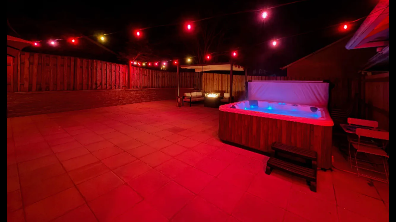 A nighttime patio features a hot tub beneath colorful string lights.