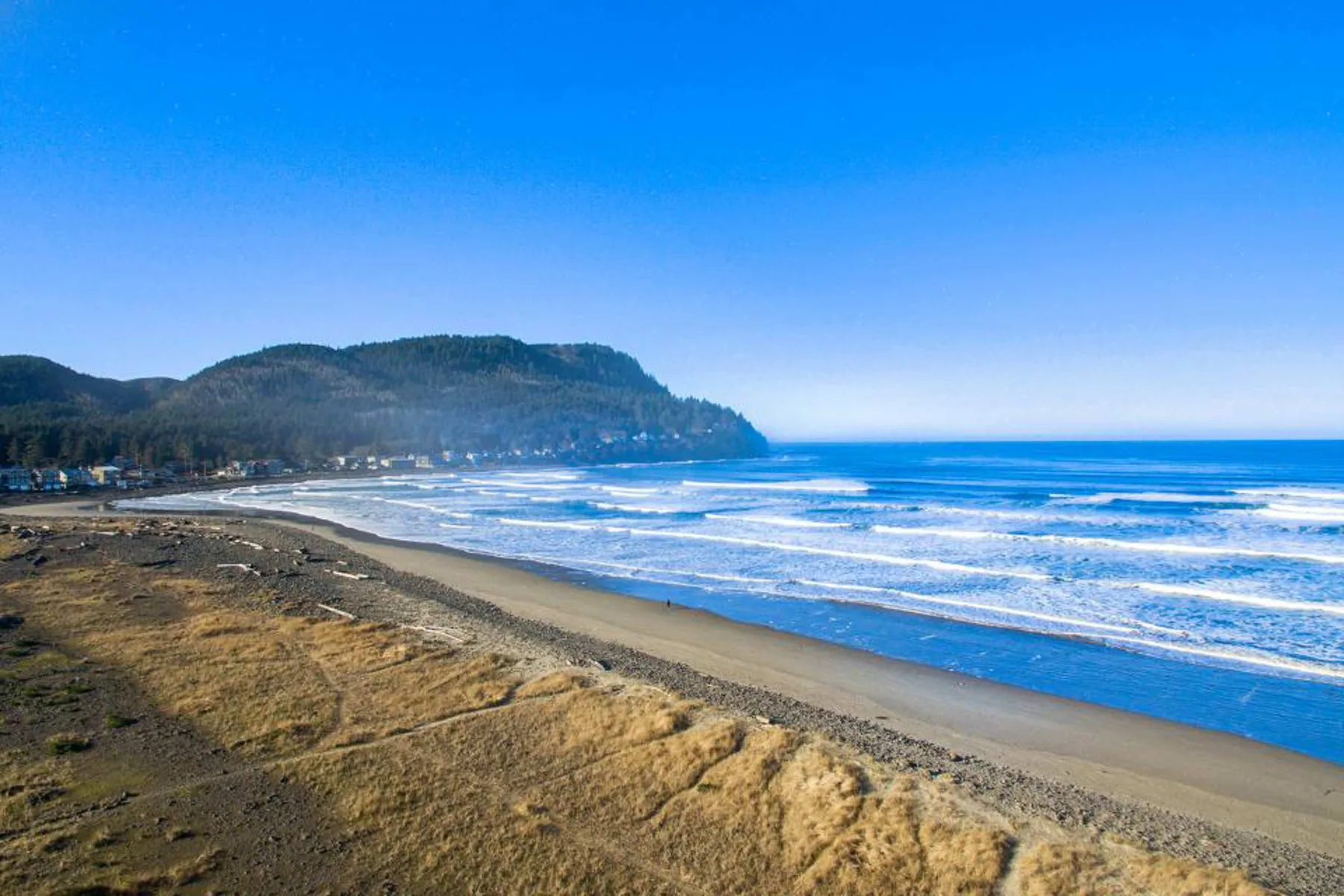 A sandy beach borders blue ocean waves, with hills along the coast.