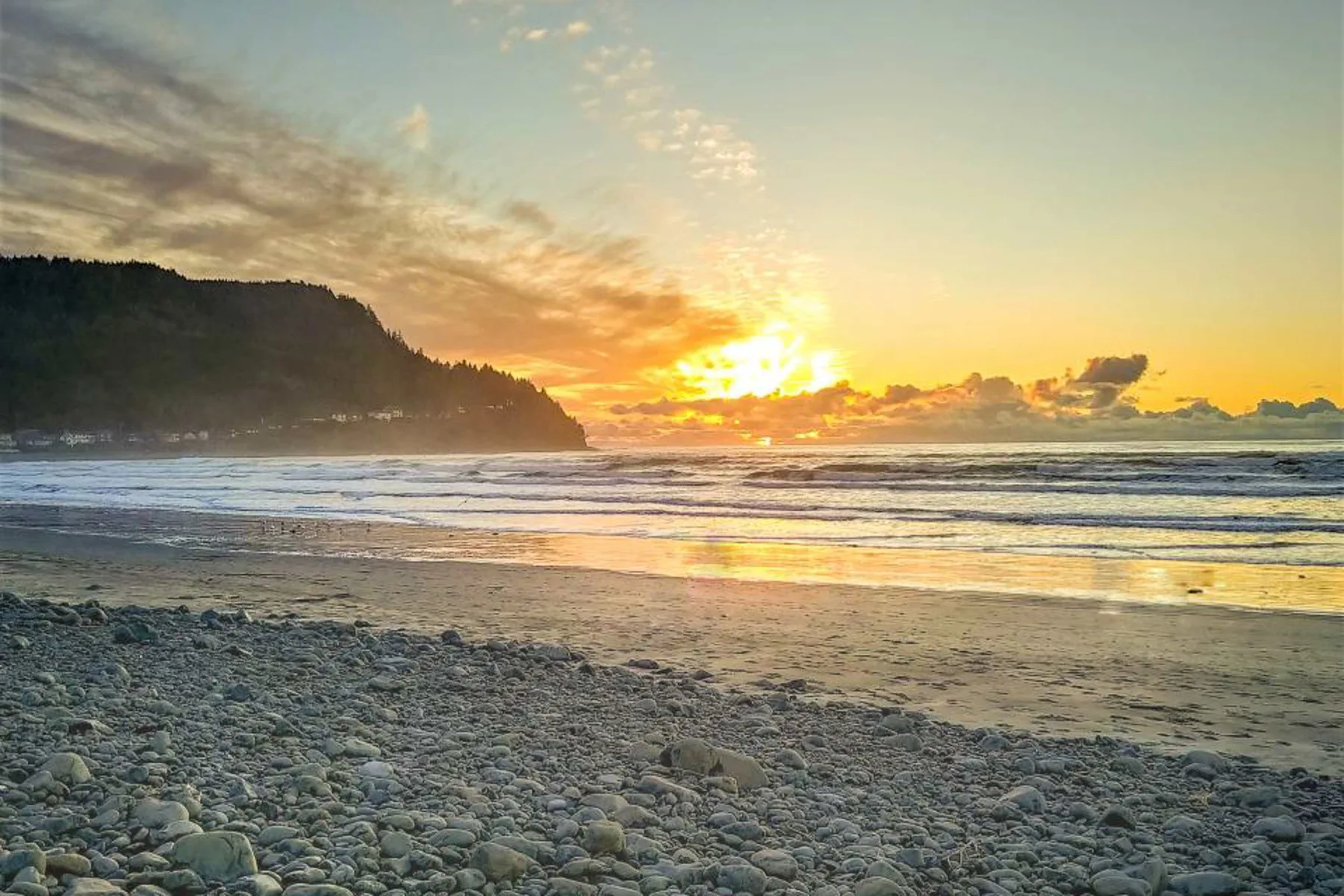 A pebble beach meets the ocean beneath a colorful sunset.