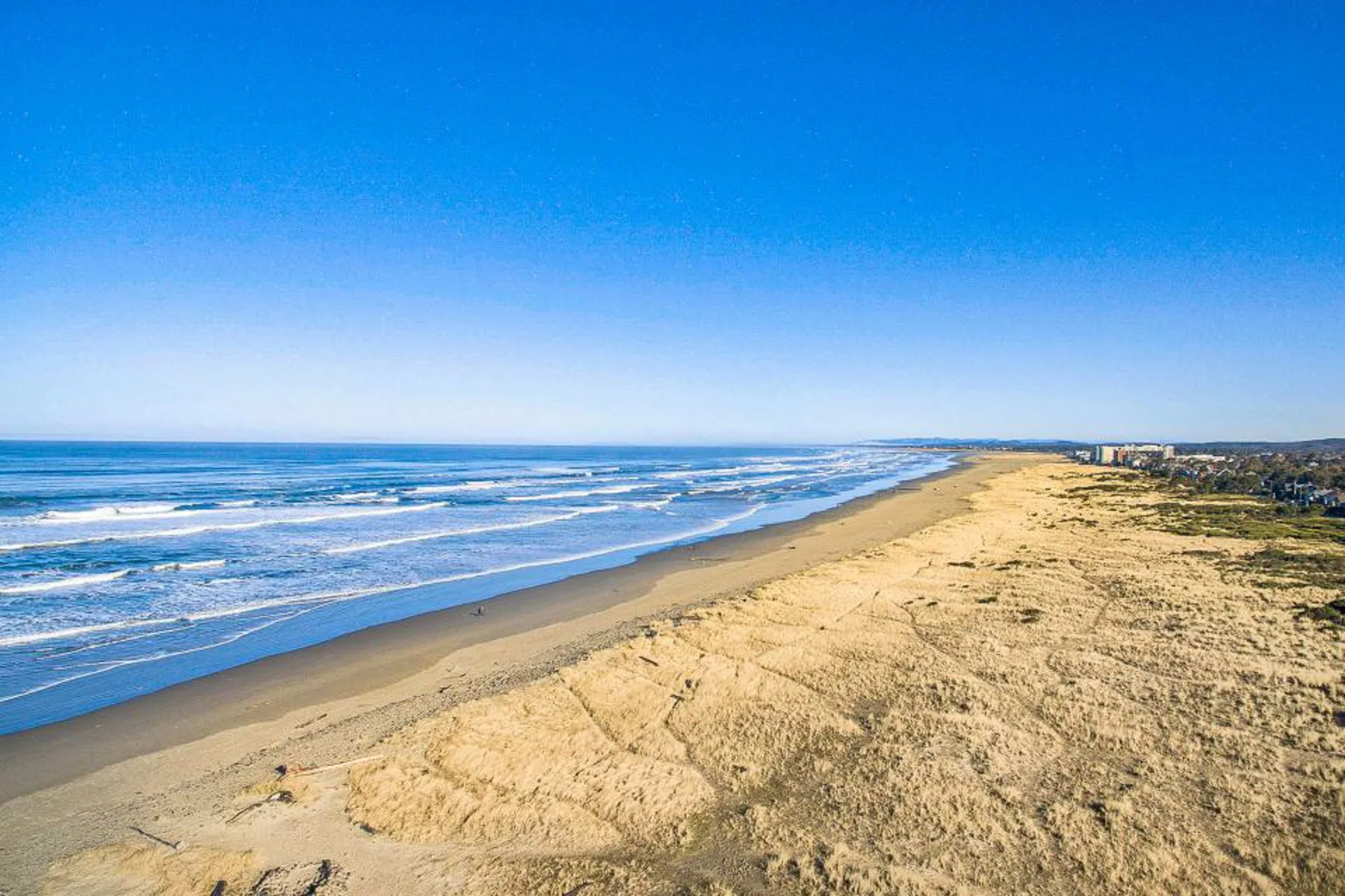 A wide sandy beach stretches beside the ocean under a clear blue sky.