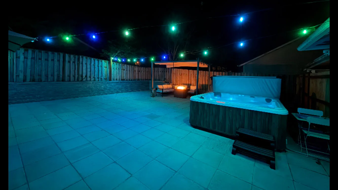 An outdoor patio at night features a hot tub beneath colorful string lights.