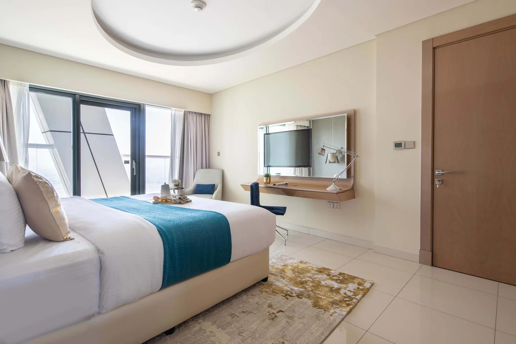 Un dormitorio luminoso con una cama, grandes ventanas y un televisor en la pared.