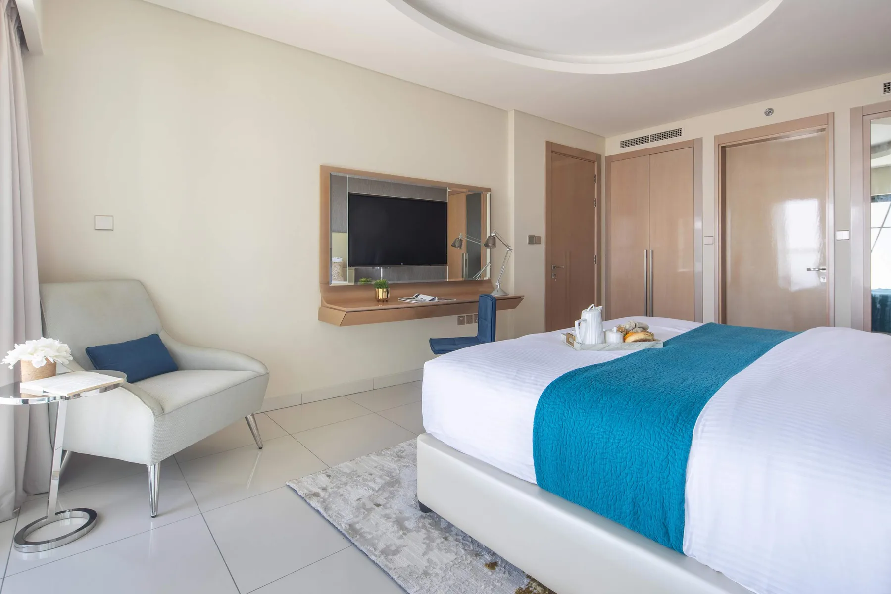 Un dormitorio luminoso con una cama, un televisor en la pared y una zona de estar.