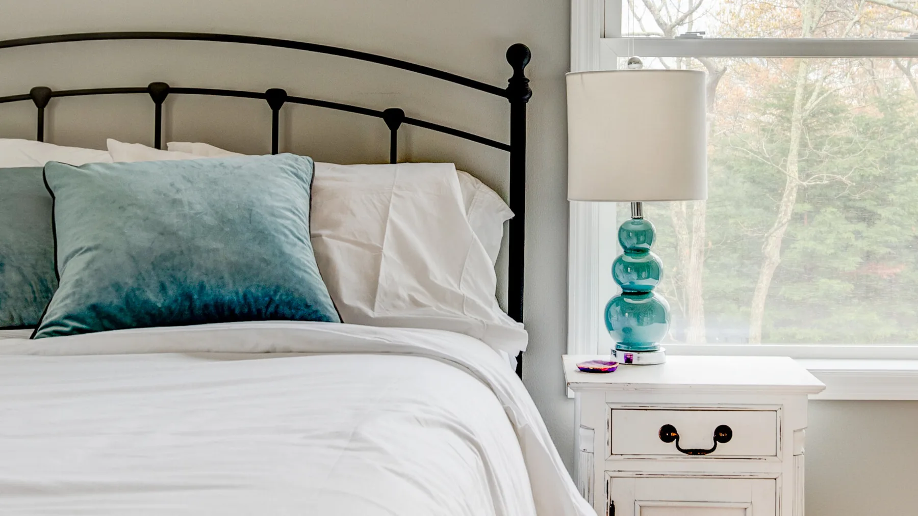 A bedroom with a neatly made bed and a bedside table beside the window.