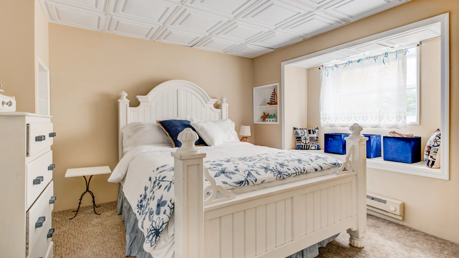 A bedroom with a large bed, blue-and-white bedding, and a bright window nook.