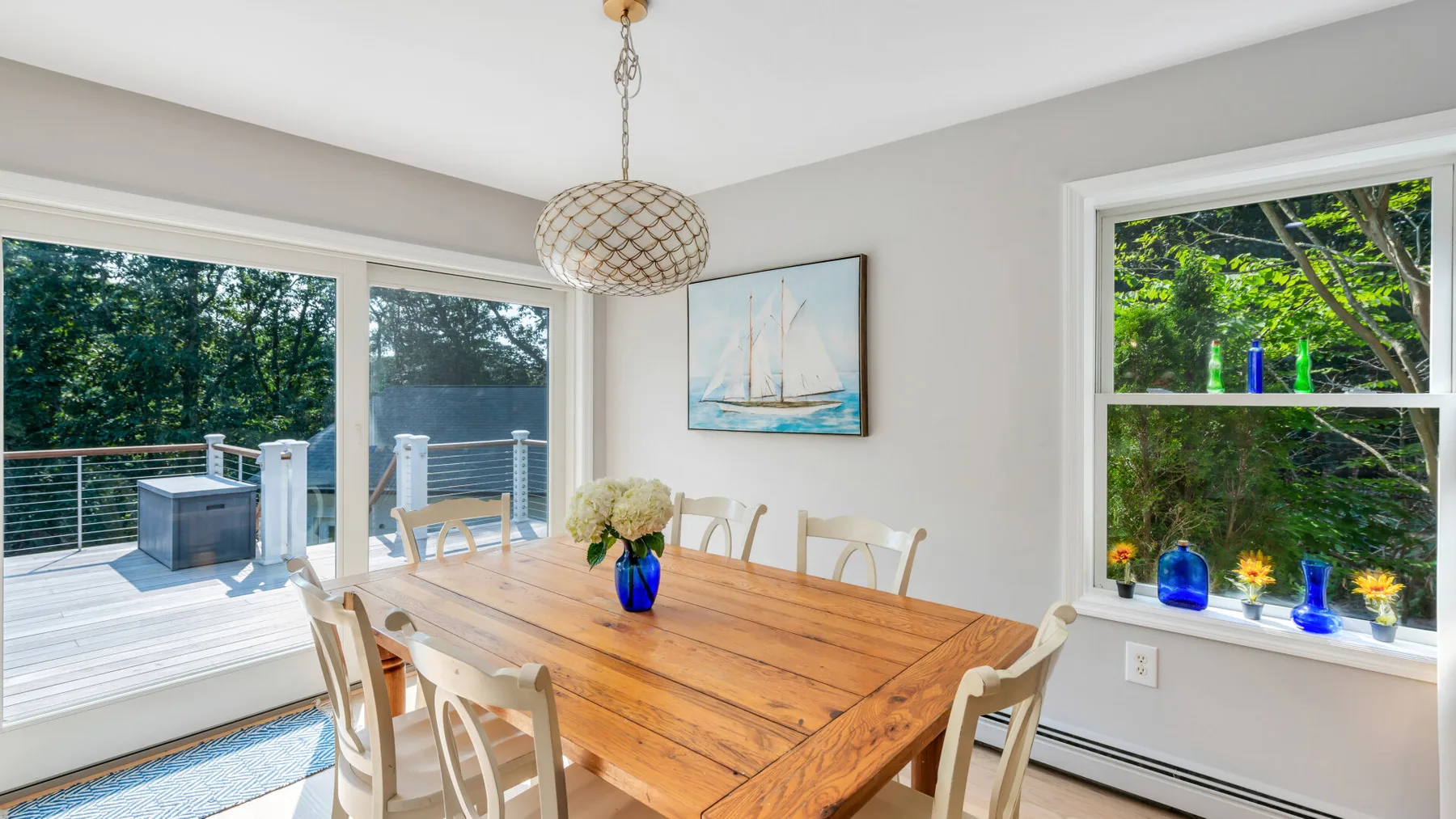 A dining area with a wooden table and chairs beside large windows.