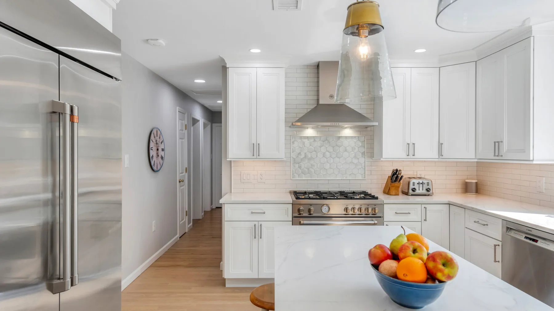 A bright white kitchen with stainless steel appliances and a fruit bowl on the island.