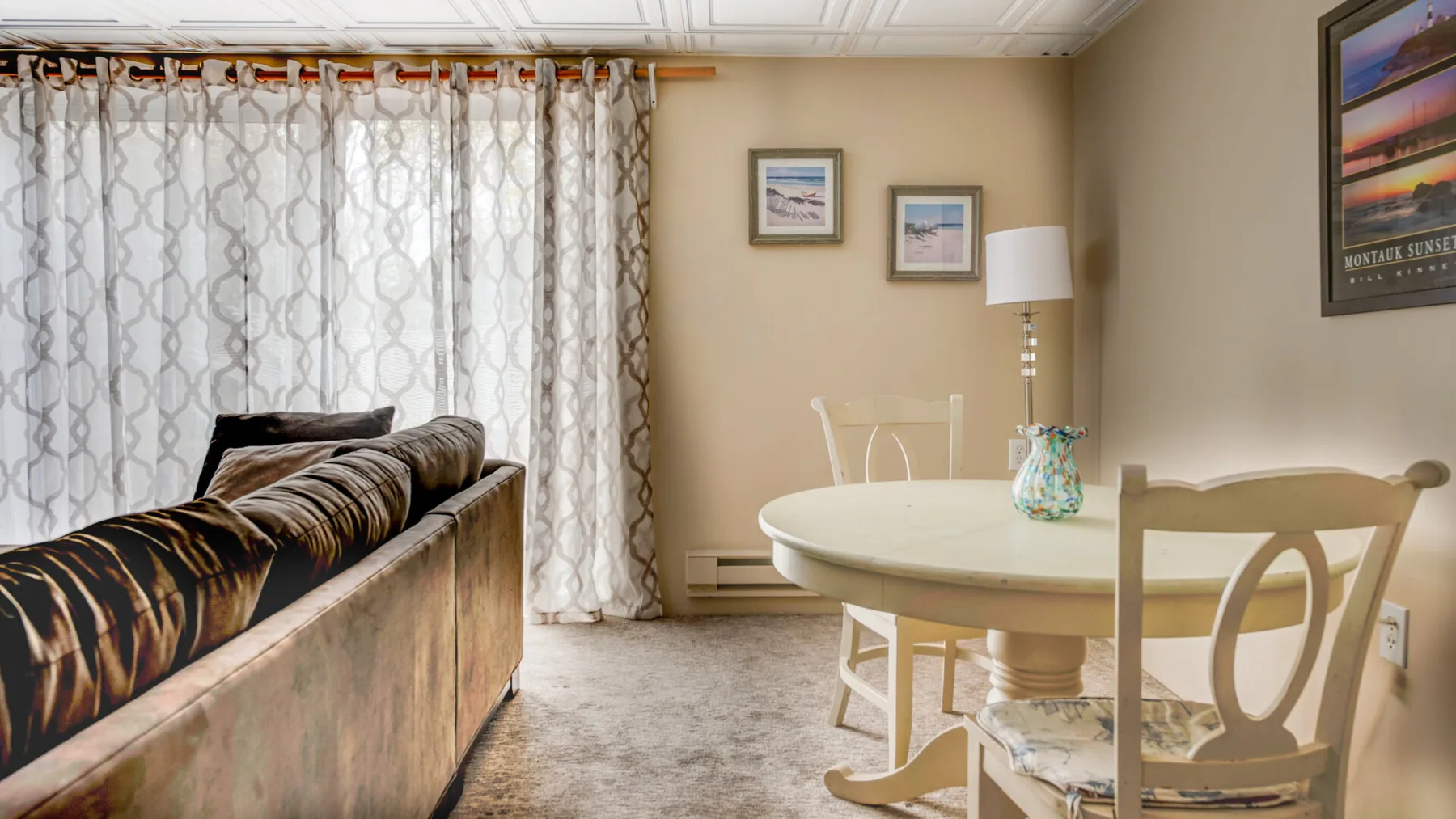 A dining area with a round table and chairs beside a curtained window.
