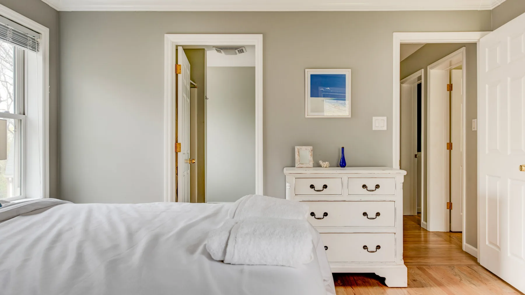 A bedroom with a bed, dresser, and open doorways.