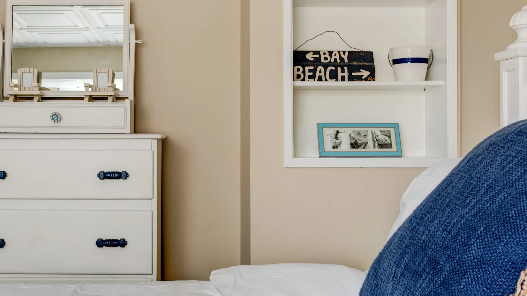 A bedroom with a white bed, dresser, and built-in wall shelves.