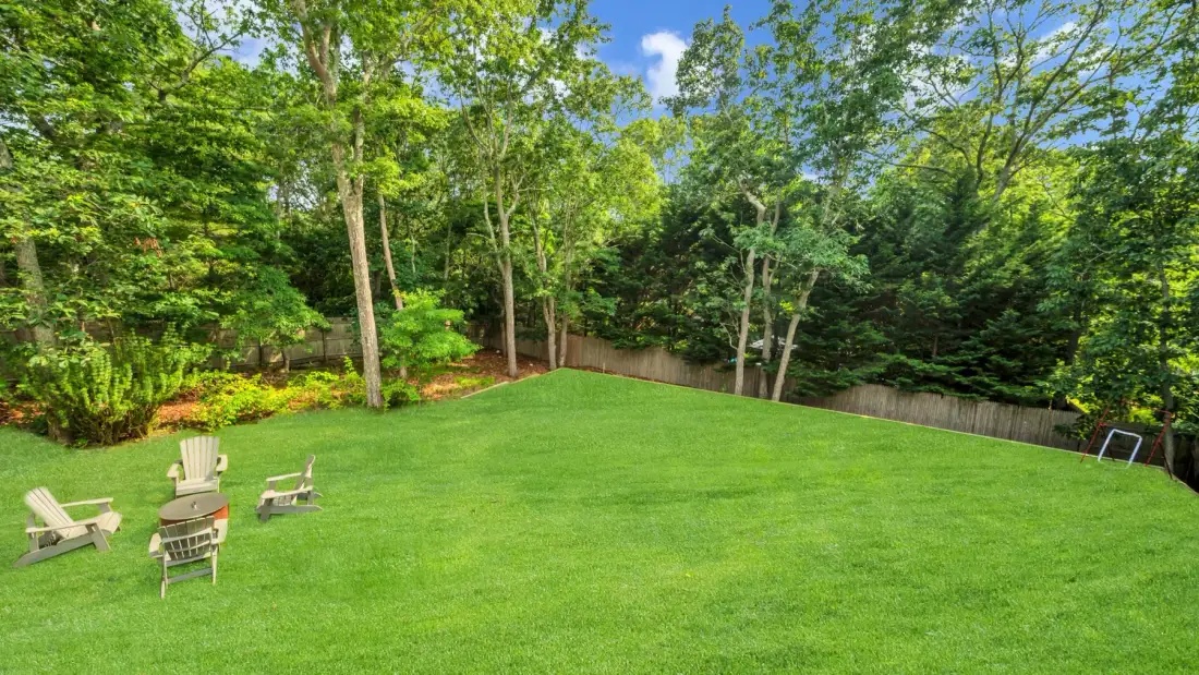 A spacious green lawn is bordered by leafy trees and a few outdoor seats.