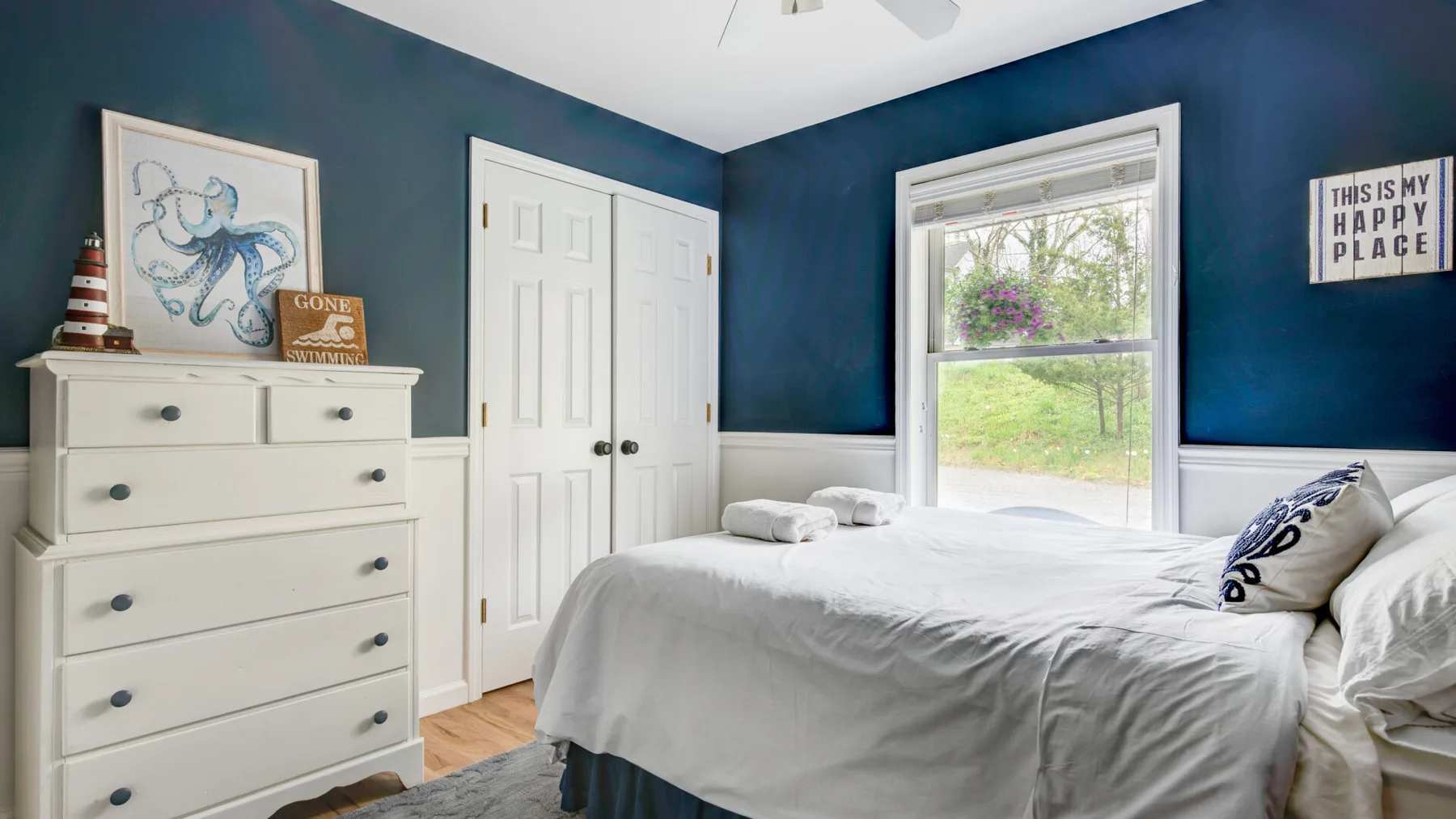 A bedroom with a white bed, dresser, and dark blue walls.