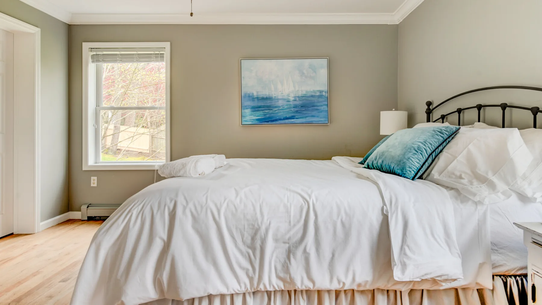 A bedroom with a bed dressed in white linens and a blue accent pillow.