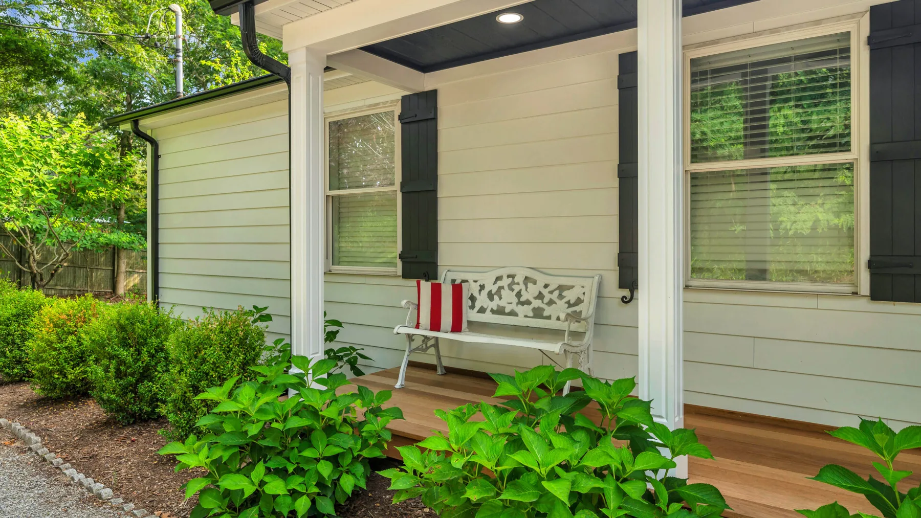 A covered porch with a bench and leafy shrubs along the edge.