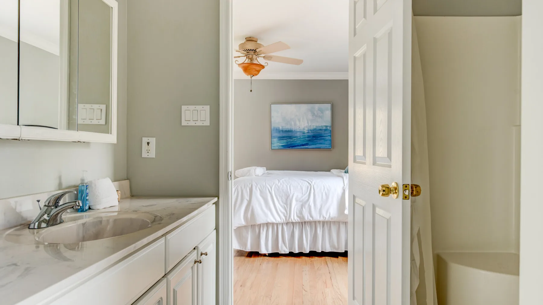 A bathroom vanity opens onto a bedroom with a neatly made bed.
