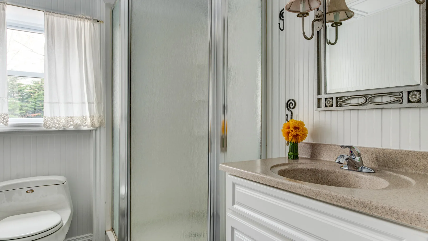 A bathroom with a sink vanity, shower, and toilet beside a window.