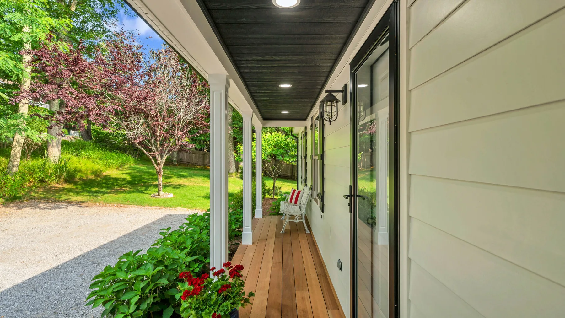 A covered porch with a wooden walkway overlooks a green yard.