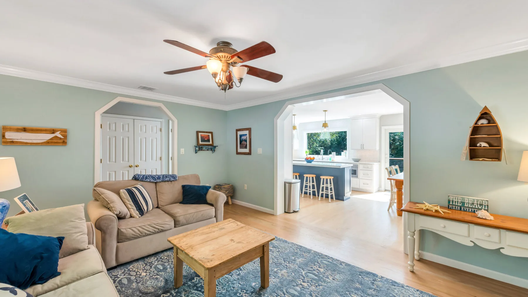 A living room with seating around a wooden coffee table, open to a bright kitchen.